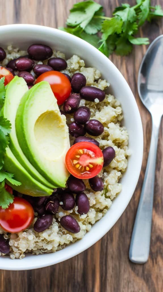 A delicious quinoa and black bean breakfast bowl with avocado slices and fresh herbs.