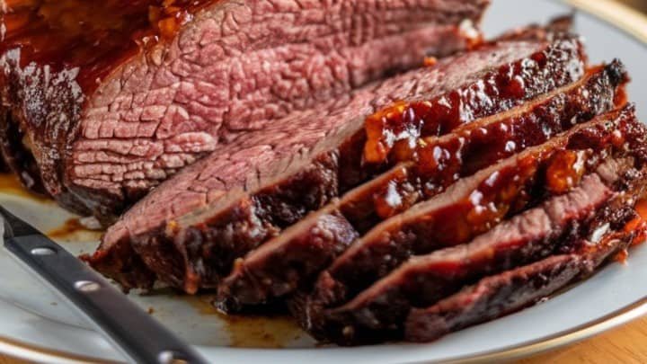 Sliced roast beef on a white plate, glistening with a rich, dark glaze. The juicy, tender meat is arranged beside a sharp knife, evoking mouthwatering appeal.