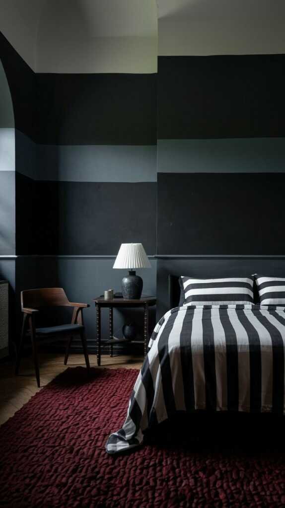 A dark bedroom featuring layered bedding in various shades of gray and white, with a plant in the corner.