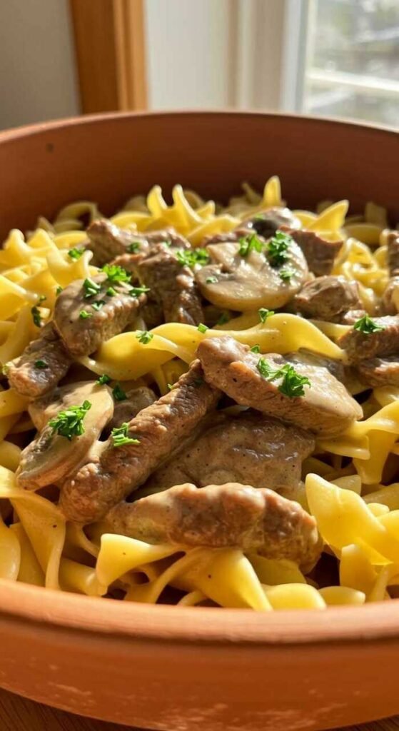A delicious bowl of beef stroganoff with egg noodles, featuring tender beef, mushrooms, and a creamy sauce.