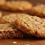 maple cinnamon oatmeal cookies on a wooden table, one with a bite taken out. The cookies appear golden-brown, conveying a warm and freshly baked tone.