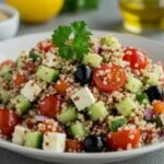 A colorful quinoa salad with cherry tomatoes, cucumber, feta, and olives on a white plate. Garnished with parsley. Fresh and healthy vibe.