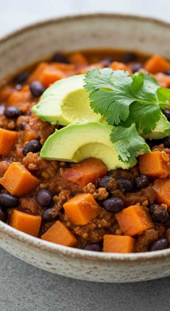 A bowl of colorful Sweet Potato and Black Bean Chili topped with avocado and cilantro.