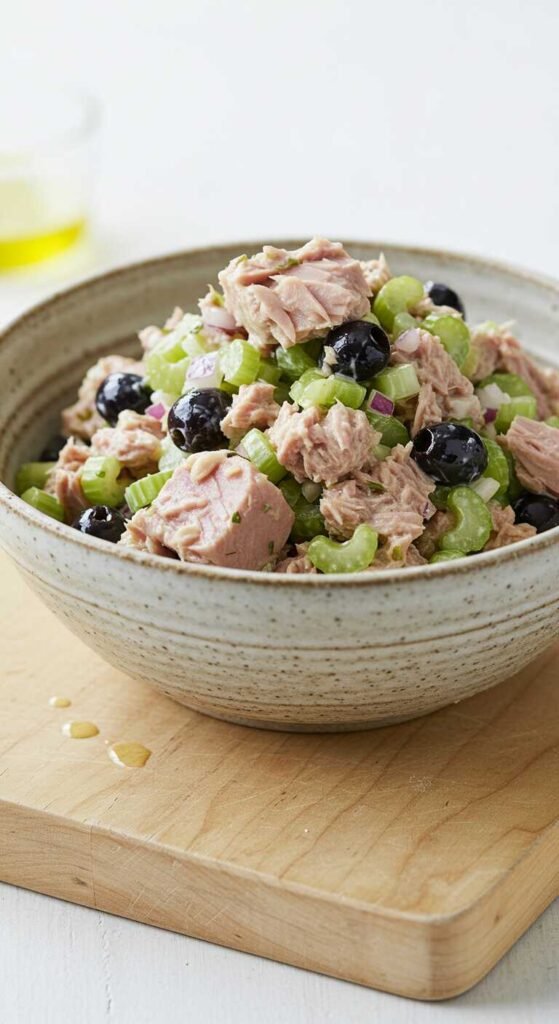 A bowl of tuna salad with olives, garnished with green herbs and served with chopped celery