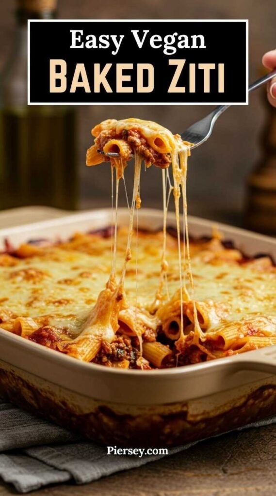 A fork lifts cheesy rigatoni from a dish of vegan baked ziti, with melted cheese strands stretching. The dish looks creamy and appetizing.