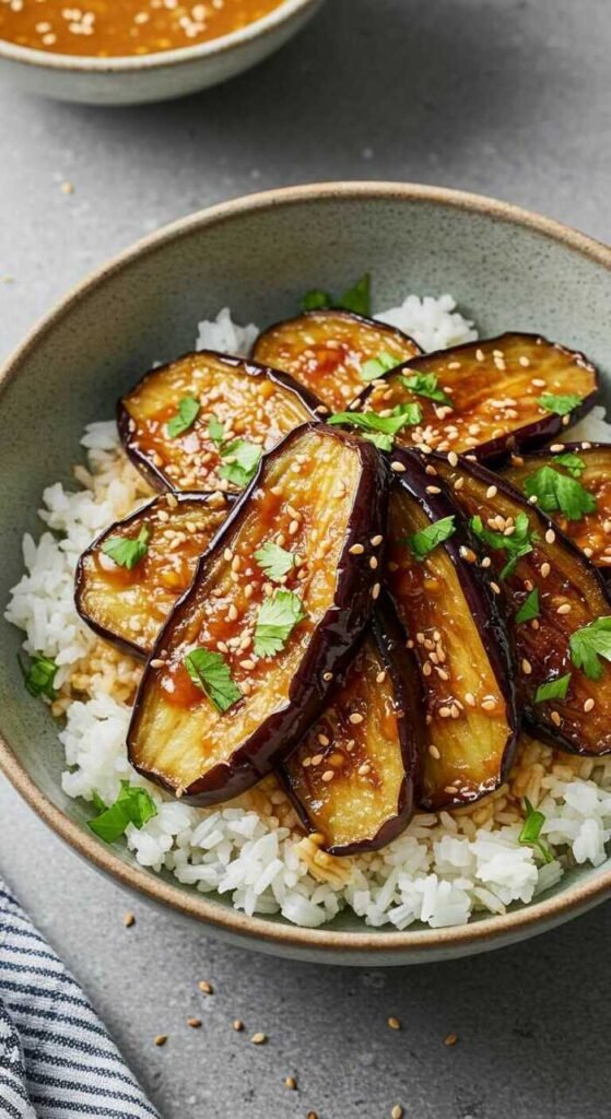 Miso Glazed Eggplant Rice Bowl with roasted eggplant slices on rice, garnished with herbs and sesame seeds.