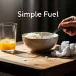 How I Eat for $2.50 a Day and Lose Weight Hand holding a spoon above a bowl of rice on a wooden table, next to a glass of orange juice. The words "Simple Fuel" appear above, conveying a minimalist tone.