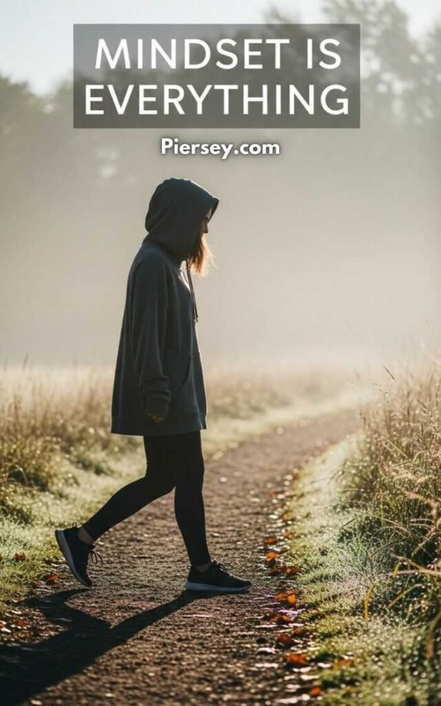 A person in a hoodie walks along a misty, tree-lined path. The calm morning light creates a serene atmosphere. Text above reads "Mindset is Everything."